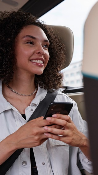 Junge Frau sitzt im Shuttlebus und schaut auf ihr Smartphone – Symbolbild für moderne Mobilität und digitale Vernetzung.