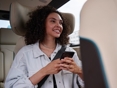 Junge Frau sitzt im Shuttlebus und schaut auf ihr Smartphone – Symbolbild für moderne Mobilität und digitale Vernetzung.