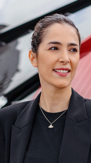 Weibliche Mitarbeiterin vor einer modernen, blütenförmigen Solaranlage auf einem Außengelände, Symbol für innovative Energieerzeugung und nachhaltige Technologie.
