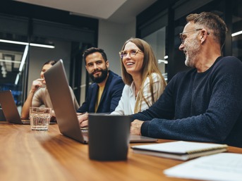 Teammeeting in modernem Büro: Mehrere Kollegen arbeiten gemeinsam an Laptops und führen ein Gespräch – Symbol für effiziente Zusammenarbeit und modernes Business.