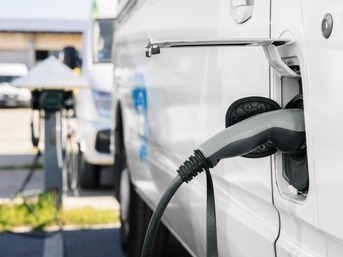 Nahaufnahme eines Elektro-Transporters, der an einer Ladestation geladen wird – Symbol für E-Mobilität und nachhaltige Fahrzeugflotten.