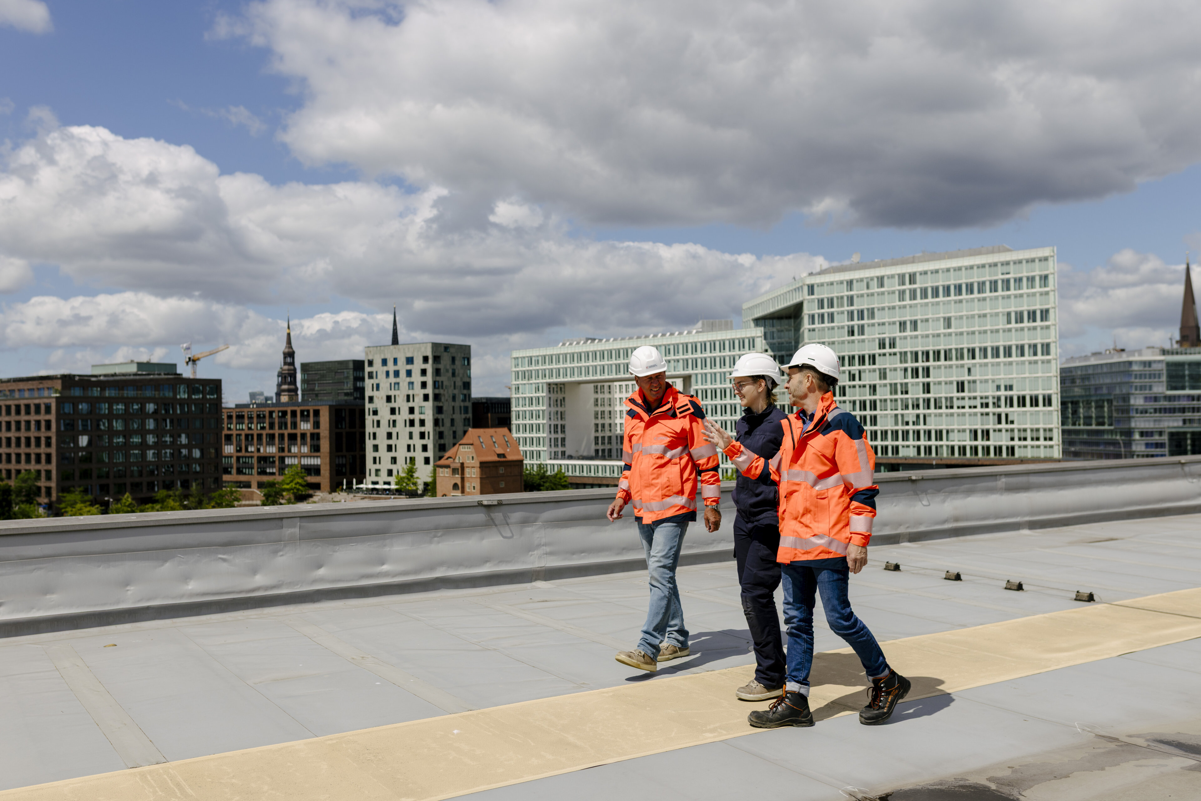 Eine Mitarbeiterin und zwei Mitarbeiter der Hamburger Energienetze in Arbeitskleidung auf dem Dach des Umspannwerks HafenCity.